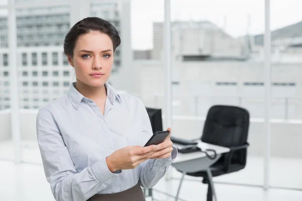 Mulher de negócios séria segurando telefone celular no escritório — Fotografia de Stock