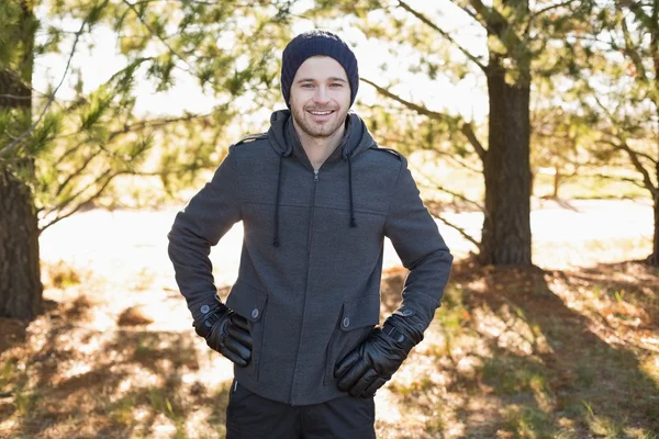 Lächelnder junger Mann in warmer Kleidung steht im Wald — Stockfoto