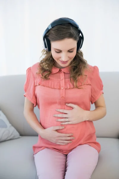 Kobieta w ciąży wspaniały słuchając muzyki, siedząc w pokoju dziennym — Zdjęcie stockowe