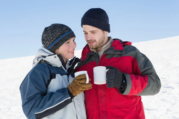 Paar in warme kleding met koffie cups op sneeuw — Stockfoto