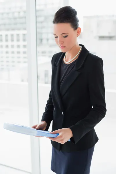 Businesswoman with folder standing against office glass wall — Stock Photo, Image