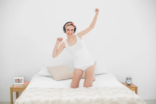 Young woman kneeling on her bed and listening to music — Stock Photo, Image