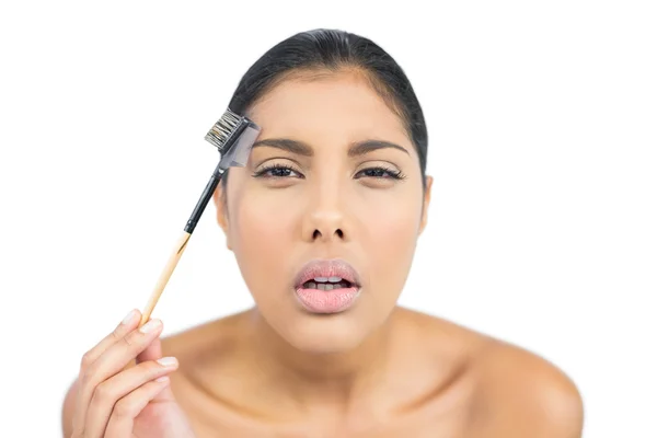 Frowning nude brunette using eyebrow brush — Stock Photo, Image