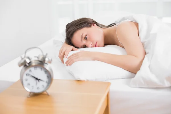 Mujer en la cama con despertador en la mesita de noche —  Fotos de Stock