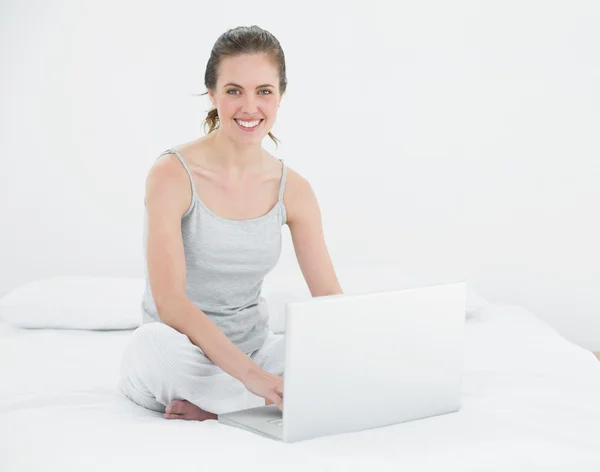 Retrato de uma mulher casual sorridente com laptop na cama — Fotografia de Stock