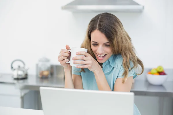 Mujer hermosa divertida usando su cuaderno mientras sostiene una taza —  Fotos de Stock