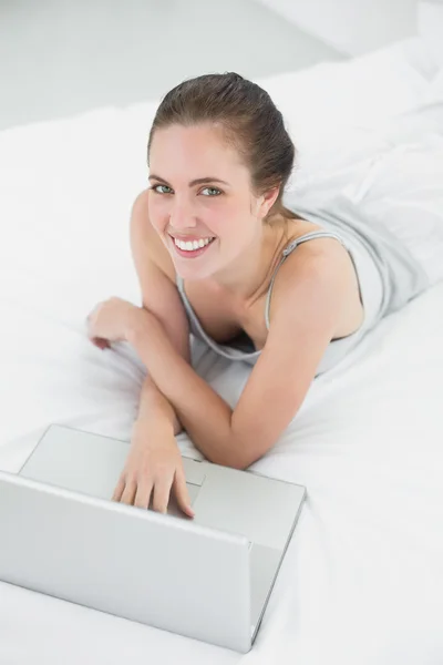 Sorridente donna casuale utilizzando il computer portatile a letto — Foto Stock