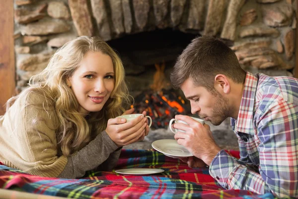 Pareja con tazas de té frente a la chimenea encendida — Foto de Stock