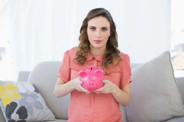 Cute pregnant woman holding a piggy bank while sitting on couch — Stock Photo, Image