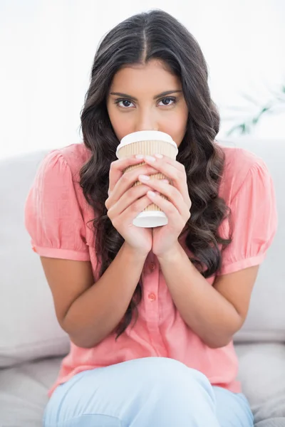 Calma linda morena sentada en el sofá bebiendo de la taza desechable —  Fotos de Stock