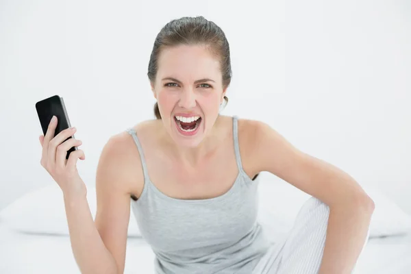 Mujer enojada gritando con el teléfono móvil en la mano en la cama —  Fotos de Stock