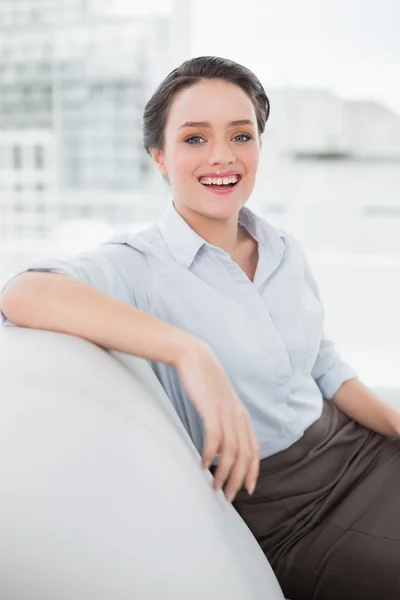 Sonriente joven bien vestida sentada en el sofá — Foto de Stock