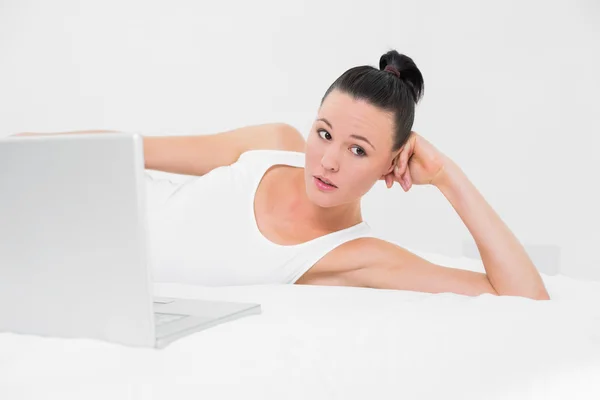 Tankeväckande casual kvinna med laptop i sängen — Stockfoto