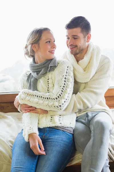 Couple in winter clothing sitting against window — Stock Photo, Image