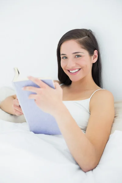 Portret van een lachende vrouw met boek in bed — Stockfoto