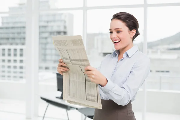 Vrolijke zakenvrouw lezen van de krant in office — Stockfoto