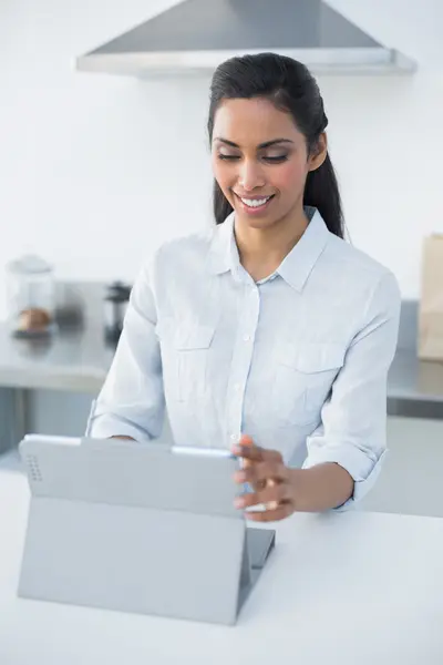 Lovely smiling woman using her tablet standing in bright kitchen — Stock Photo, Image