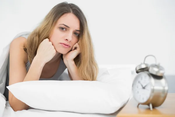 Serious brunette woman lying on her bed under the cover — Stock Photo, Image