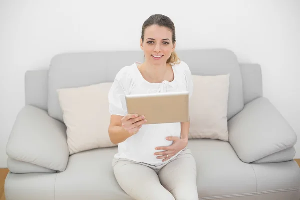 Mulher grávida tocando sua barriga enquanto segurando seu tablet — Fotografia de Stock