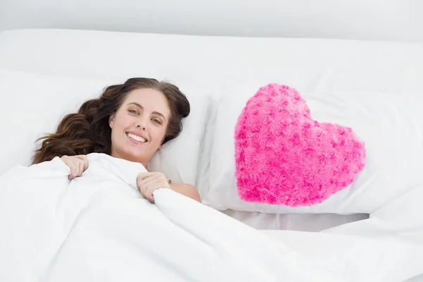 Mujer sonriente acostada en la cama con funda de almohada en forma de corazón — Foto de Stock