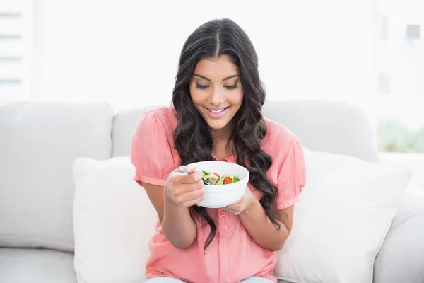 Zufriedene süße Brünette sitzt auf der Couch mit Salatschüssel — Stockfoto