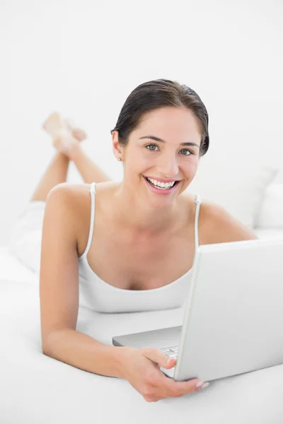 Retrato de una mujer casual sonriente usando un portátil en la cama —  Fotos de Stock