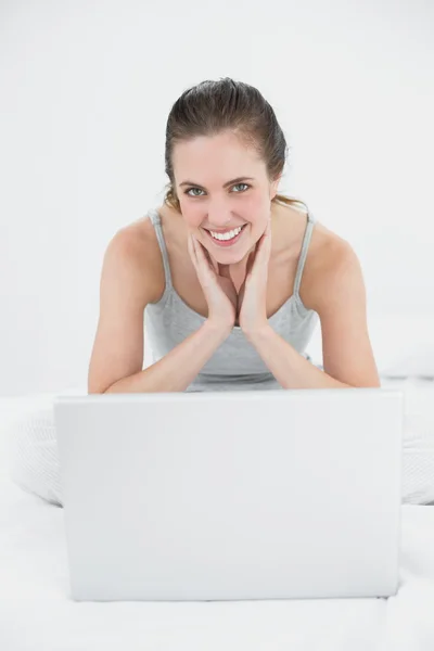 Retrato de uma mulher casual sorridente com laptop sentado na cama — Fotografia de Stock