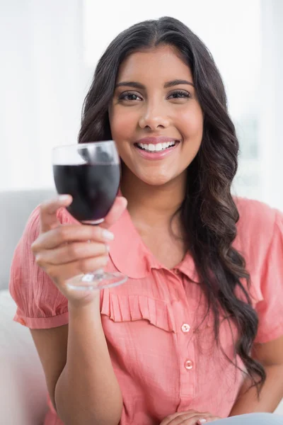 Glad söt brunett sitter på soffan håller glas vin — Stockfoto