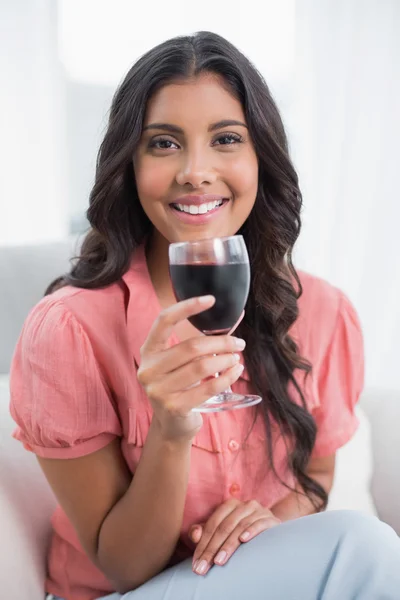 Joyeux mignon brunette assis sur le canapé tenant verre de vin — Photo