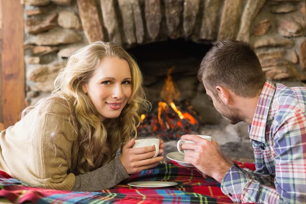 Couple with tea cups in front of lit fireplace — Stock Photo, Image