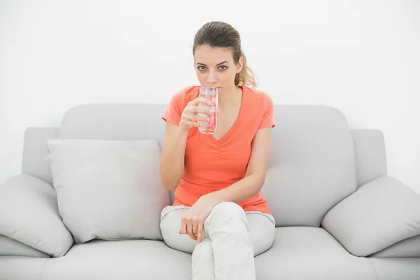 Attraktive lässige Frau, die ein Glas Wasser trinkt und in die Kamera schaut — Stockfoto