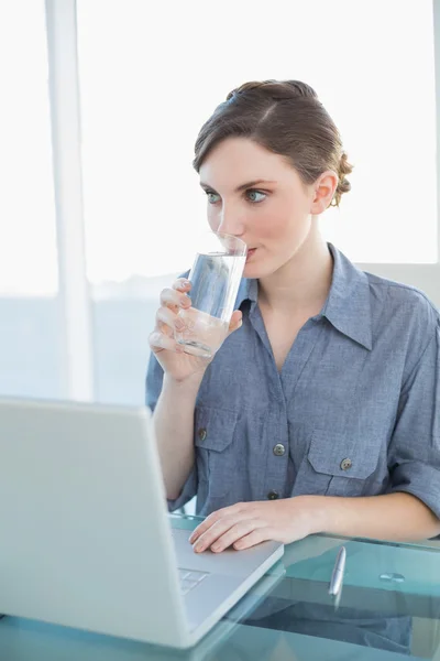 Gorgeous young businesswoman drinking a glass of water sitting at her desk — Stock Photo, Image