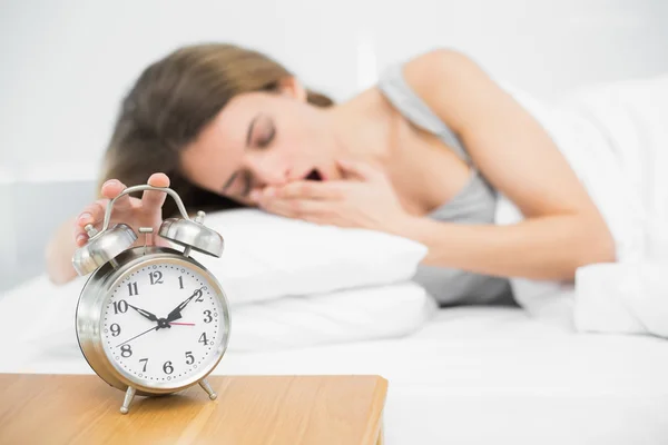 Lovely woman turning off the alarm clock lying on her bed — Stock Photo, Image