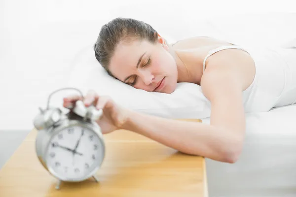 Slaperig vrouw in bed uitbreiding hand aan alarm clock Stockfoto