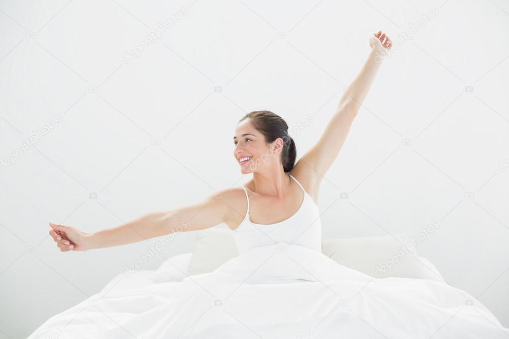 Smiling woman stretching arms in bed