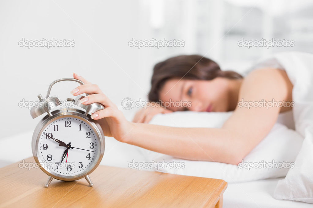 Blurred woman in bed extending hand to alarm clock