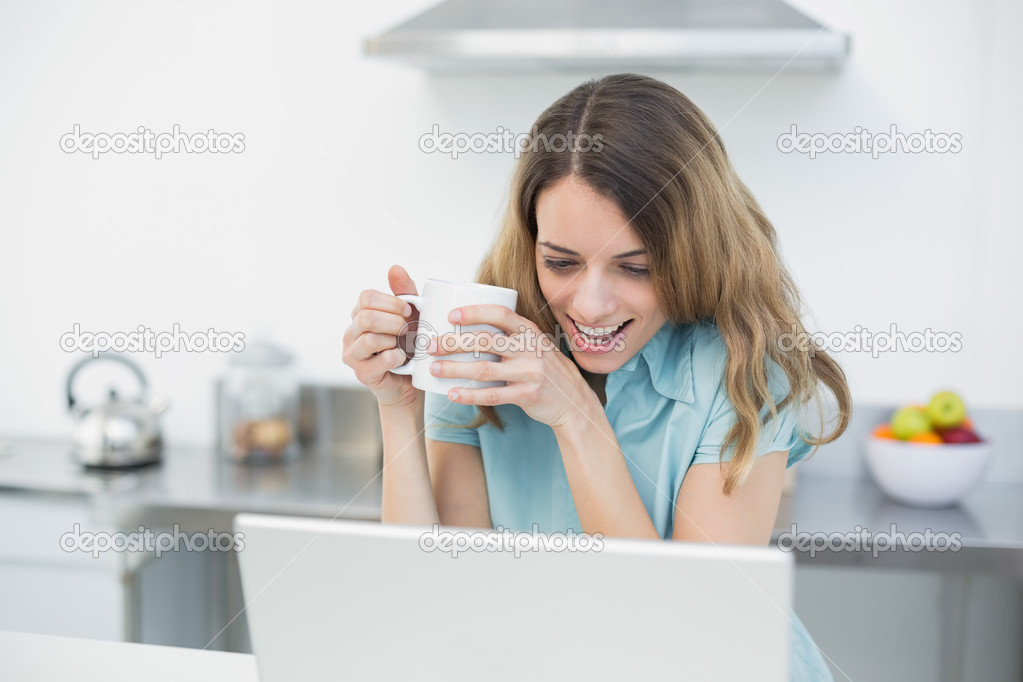 Amused beautiful woman using her notebook while holding a cup