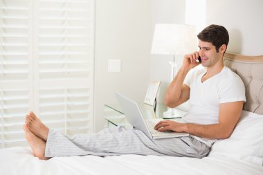 casual gülümseyen adam yatakta kullanarak cep telefonu ve laptop