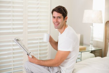 Gazetede yatakta kahve fincanı ile neşeli adam