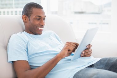 casual gülümseyen afro man dijital tablet kanepe üzerinde kullanma