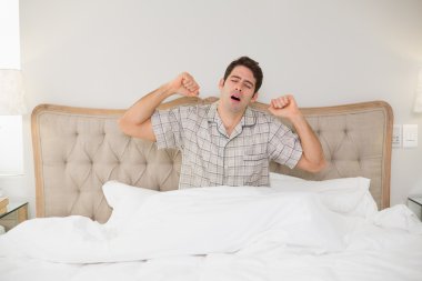 genç adam yatağında uyanmak ve kollarını esneme