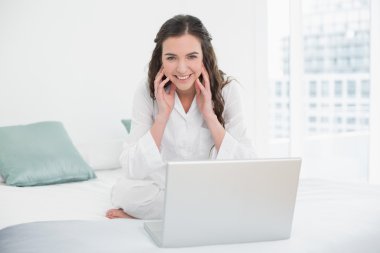 yatakta oturmuş laptop ile Casual esmer gülümseyen