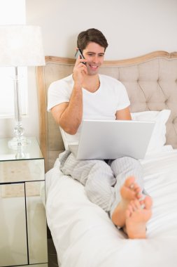 casual gülümseyen adam yatakta kullanarak cep telefonu ve laptop