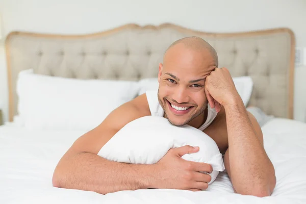 Smiling casual bald young man lying in bed — Stock Photo, Image
