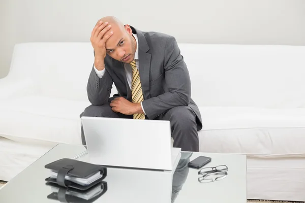 Беспокойный бизнесмен с ноутбуком, держащийся за голову дома — стоковое фото