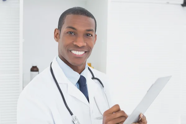 Médico sorridente escrevendo uma prescrição em consultório médico — Fotografia de Stock