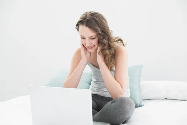 Sonriente morena casual mirando el portátil en la cama — Foto de Stock