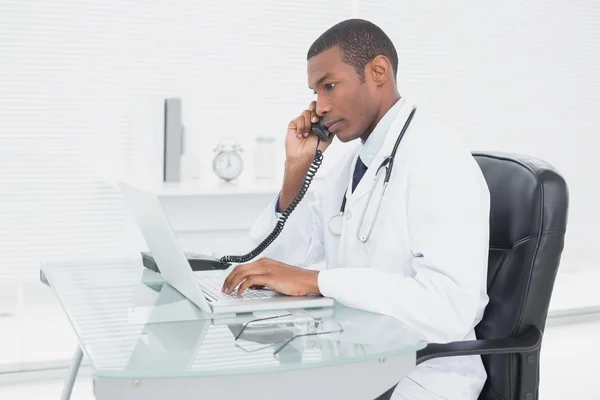 Médico masculino usando telefone e laptop no consultório médico — Fotografia de Stock