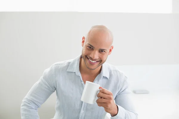 Sonriente hombre guapo sosteniendo la taza de café en casa — Foto de Stock