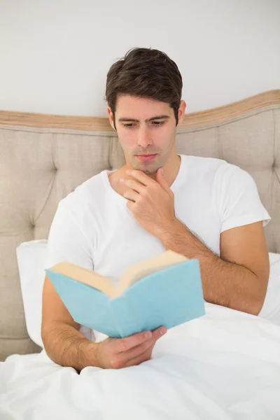 Relaxed young man reading book in bed — Stock Photo, Image